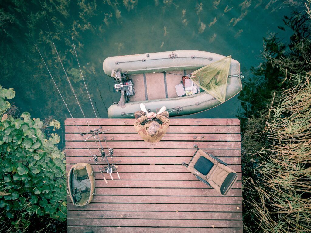 Photo prise de haut d'un ponton sur lequel un pêcheur est installé avec son matériel et son bateau.